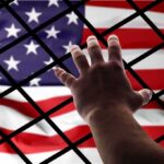 Immigrant-Only Payout Sparks Boston Firestorm Hand reaching through fence toward American flag