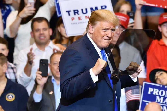 shutterstock_1148319815 Donald Trump at a rally raising his fists on stage