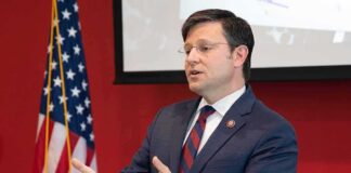 Man in suit speaking at podium with US flag in background