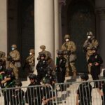 Police Union Blitz Hits LA Mayoral Race Riot police and soldiers stand guard on building steps behind barricades