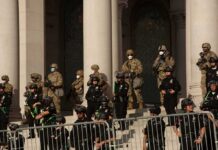 Riot police and soldiers stand guard on building steps behind barricades