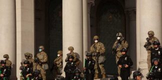 Riot police and soldiers stand guard on building steps behind barricades