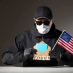 DOJ Hammers Voter Fraud Ring Person in mask and gloves holding ballot envelope and U.S. flag
