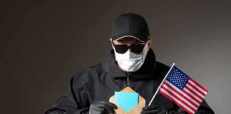 Person in mask and gloves holding ballot envelope and U.S. flag