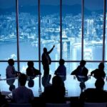 Business meeting with presenter pointing at city skyline through large windows