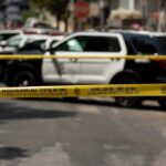 Police tape cordoning off street with patrol SUVs behind