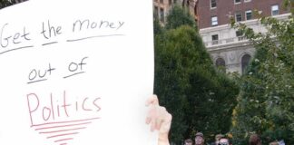 Protesters holding a large handwritten sign at a crowded outdoor rally