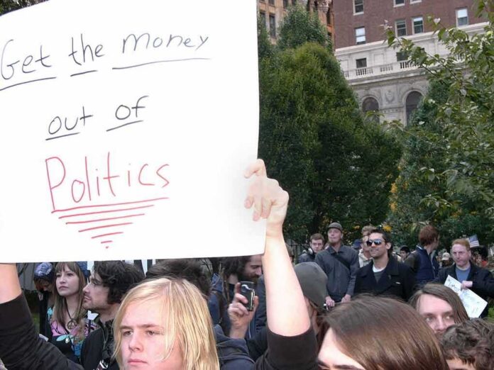 Protesters holding a large handwritten sign at a crowded outdoor rally
