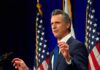 California Bill Puts Religious Neutrality To Test Man in suit speaking at podium with U.S. flags behind him