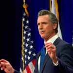 California Bill Puts Religious Neutrality To Test Man in suit speaking at podium with U.S. flags behind him