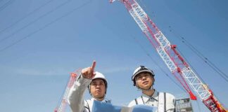 Two construction workers reviewing plans at a site with cranes