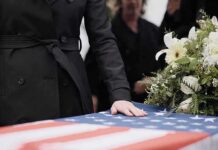 Domestic Violence Crisis Hits Home Mourner rests hand on flag-draped casket with flower arrangement
