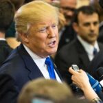 Trump’s Live Text Upends Maher Claim man in suit speaking to reporters with microphones