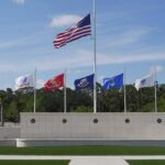 United States flag at half-mast above military branch flags at a memorial