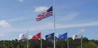United States flag at half-mast above military branch flags at a memorial
