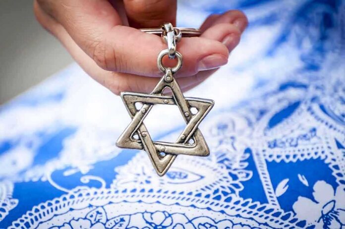 shutterstock_1166274427 Hand holding a metal Star of David pendant