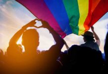 Capitol Clash Brewing Over Trans Bill Crowd under a rainbow flag at sunset