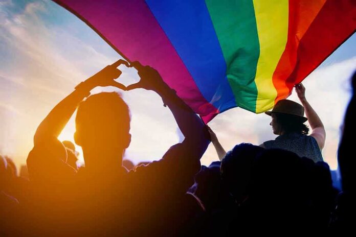 shutterstock_1177679803 Crowd under a rainbow flag at sunset