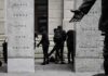 group of masked people in black clothing between granite pillars