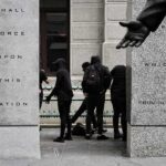 Masked Raiders Hit City Hall group of masked people in black clothing between granite pillars