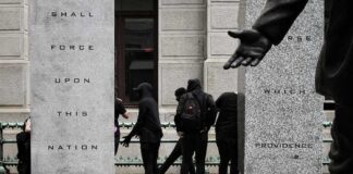 group of masked people in black clothing between granite pillars