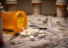 Tax Tsunami Hiding Behind “Free” Care? Prescription pill bottle and white tablets on scattered US dollar bills