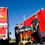 Paramedics move a patient on a stretcher between red ambulances