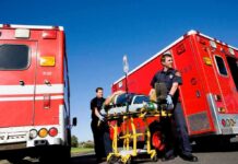 Paramedics move a patient on a stretcher between red ambulances