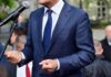 Campaign Silence Fuels ‘Discharge’ Frenzy Man in a navy suit speaking at a microphone