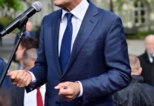 Man in a navy suit speaking at a microphone