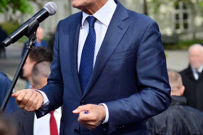 shutterstock_1392039713 Man in a navy suit speaking at a microphone