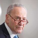 older man in suit with red glasses looking to the side