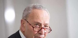 older man in suit with red glasses looking to the side
