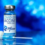 Consumer-Fraud Fight Puts Pfizer On Notice Pfizer COVID-19 vaccine vial with syringe on blue background