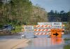 Isaias Roars In – Evacuations Loom Road closed barricades blocking a flooded rural highway with detour sign