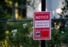 Police Dragnet Nails Wrong Driver? Red notice sign on a black pole in a leafy outdoor area