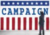 Flu Or Psych Ward? Timeline Doesn’t Add Up Man in suit writing on large campaign banner with stars and stripes